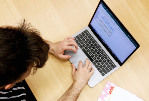 Un étudiant écrit sur le clavier de son ordinateur dans lequel on peut voir un tableau de données.