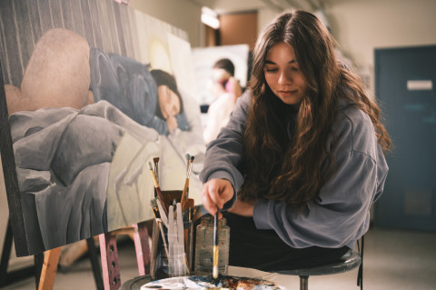 Une étudiante assise devant sa toile met de la peinture sur son pinceau
