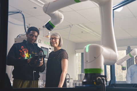 Une enseignante avec un étudiant regarde un bras robotique