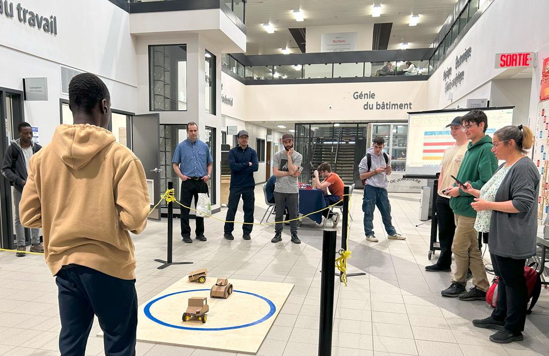 Des gens regardent l'arène au sol, qui comprend des robots en carton en action.